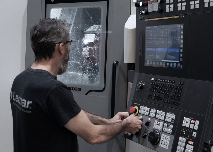 Ingeniero o responsable de producción con planos/tablet delante de una máquina CNC o línea de mecanizado